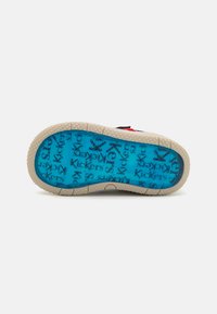 Semelle de chaussure avec un bord extérieur de couleur claire, un intérieur translucide bleu avec un motif de texte "Kickers" répété et une surface de grip texturée.