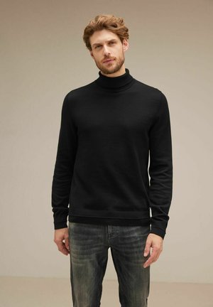 Suéter negro de cuello alto hecho de tela suave, diseño ajustado, puños y dobladillo acanalados, combinado con jeans gris desgastado. Look sencillo y discreto.