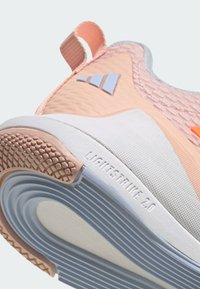 Ľahká atletická obuv s hornej časťou v ružovej a bielej farbe, textúrovaná sieťovina a gumová podrážka s modrým pruhom a drapákovým vzorom.