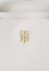 Borsa a tracolla in pelle bianca con un finish testurizzato. Presenta un accento con logo in tono oro nell'angolo in basso a sinistra. Dettagli di cucitura delicata lungo la parte superiore.