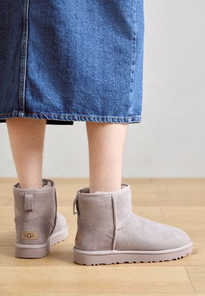 Graue Wildleder-Ankle Boots mit weichem Futter, flacher Sohle und kleinem Absatz. Verfügt über eine Schlaufe an der Rückseite und ein markiertes Etikett an der Seite.