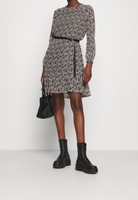 Zwart-witte bloemenjurk met lange mouwen, een ceintuurlijn en een flared zoom. Gecombineerd met zwarte veterschoenen tot de enkel en een kleine tas.