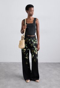 Svart tank topp med firkantet utringning, bukser med blomstermønster i svart og grønne detaljer, samt en liten vevd stråveske. Beige slip-on sko.