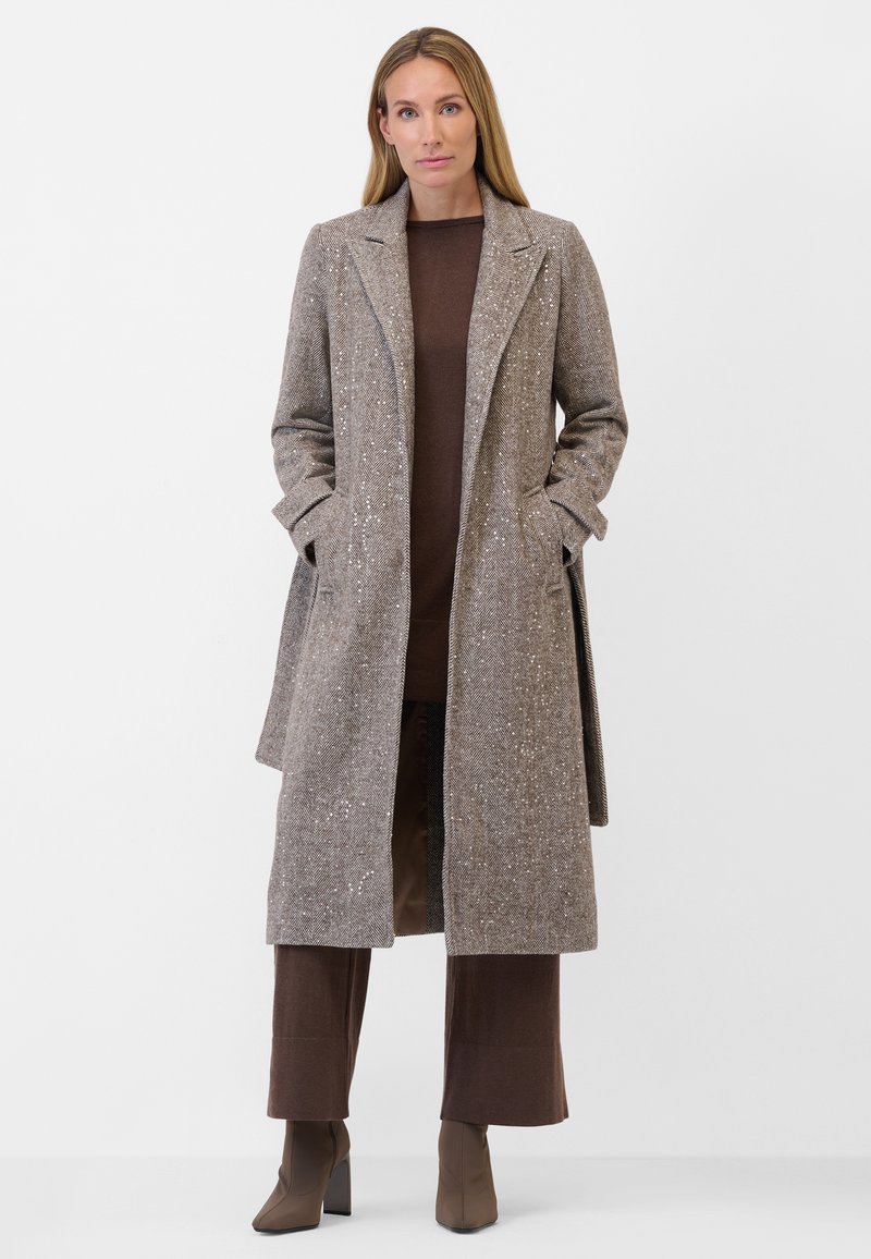 Lång, brun, texturerad kappa med ett subtilt mönster, notchad krage och sidofickor, bärs över en matchande brun topp och vida byxor.