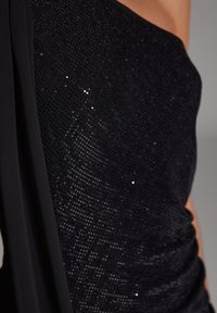 Svart paljettkjole med tettsittende bodice og glattere drapering; har subtil glans fra paljettene og en strukturert utringning med stropper.
