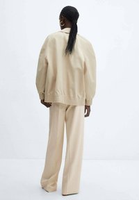 Beige bomber jacket with a ribbed hem, paired with wide-leg beige pants. Smooth fabric texture and casual design, viewed from the back.