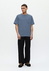 T-shirt de algodão azul com design básico, mangas curtas e bolso no peito, combinado com calças largas pretas e sapatos castanhos.