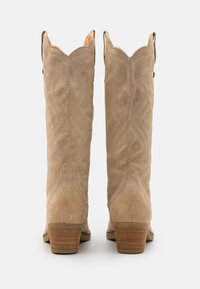 Sandfarbene Wildleder-Westerngymnastikstiefel mit spitzem Zehenbereich, gewelltem Schaft und aufwendiger tonaler Stickerei. Der niedrige, gestapelte Absatz sorgt für Stabilität.