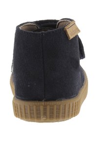 Bottines en suède bleu marine avec une semelle en caoutchouc texturé, présentant une couture à l'arrière et une étiquette logo marron sur le talon.