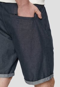 Shorts en denim de couleur bleu marine foncé avec des ourlets roulés gris clair, dotés d'une poche latérale et d'une texture lisse, adaptés à une tenue décontractée.