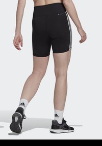 Czarne szorty sportowe z wysokim stanem, białymi bocznymi paskami i dopasowanym krojem. Noszone z czarnymi sneakerami i białymi skarpetkami do kostek.