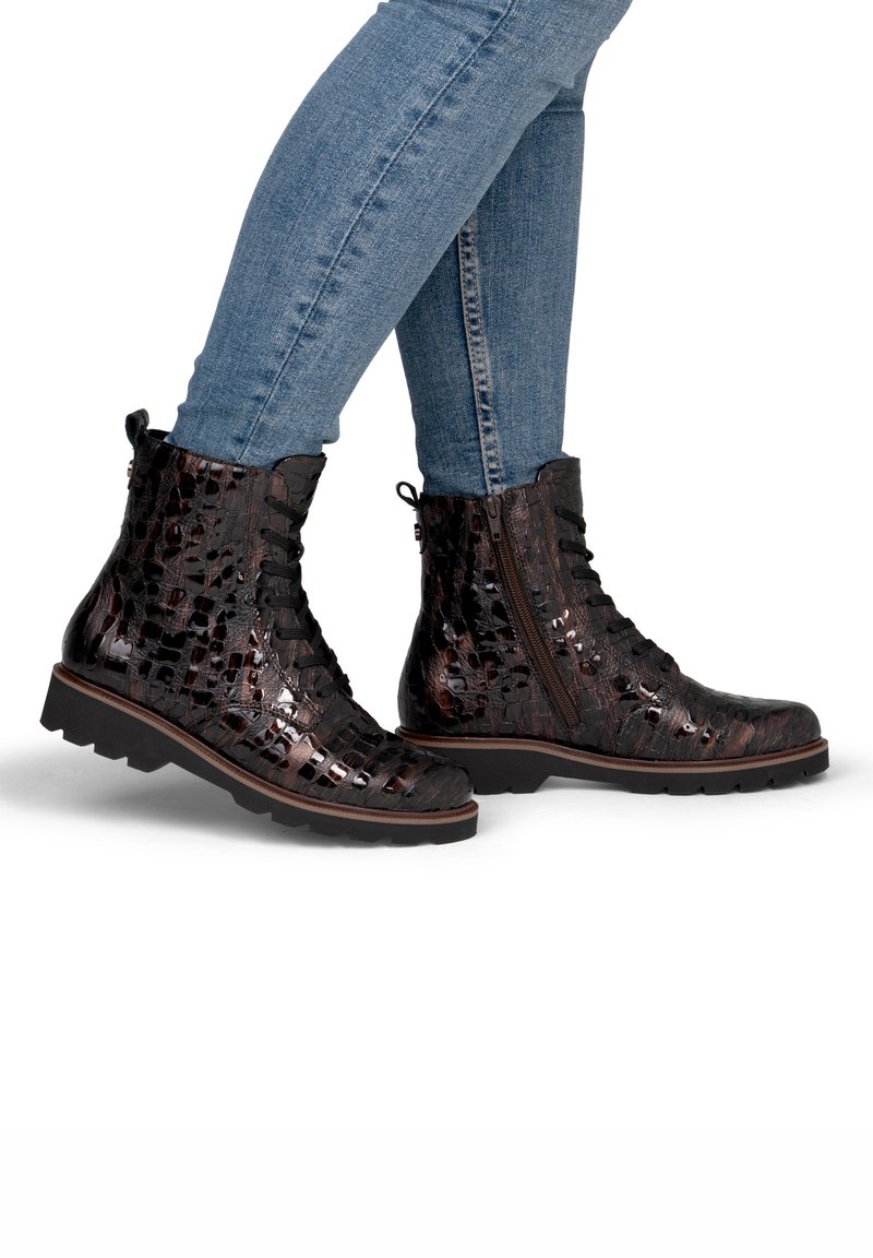 Bottines montantes lacées brillantes marron foncé à motif crocodile avec fermeture éclair latérale, portées avec un jean bleu ajusté.