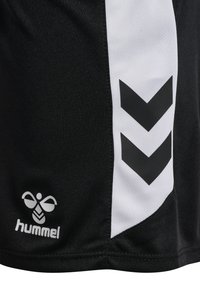 Svarta atletiska shorts med en vit sidoremsa, som har svarta vinklar och en vit logotyp från Hummel längst ner till vänster.