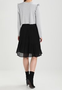 Grå kortärmad tröja med volangdetaljer, kombinerad med en knälång svart plisserad kjol. Svarta ankelskor med en glansig yta.