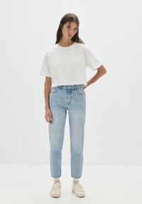 Fehér, rövidített póló, világoskék, magasderekú farmernadrág és bézs sportcipő. Egyszerű kialakítás rövid ujjakkal, egyenes szabással és világos mosott farmer anyagból.