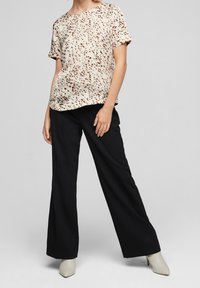 Haut beige avec un motif moucheté marron, manches courtes et encolure ronde, associé à un pantalon noir taille haute à jambes larges et des talons beiges pointus.