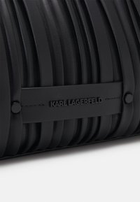Sac à main en cuir noir texturé avec des plis verticaux, doté d'une bandoulière lisse embossée "KARL LAGERFELD" et d'accents en métal noir.