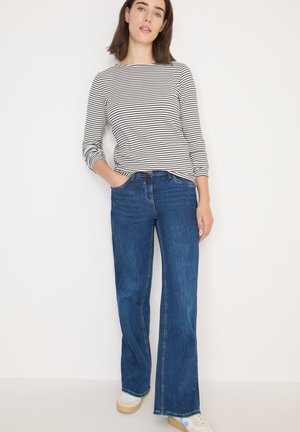 Gestreepte longsleeve top in zwart en wit; blauwe wijde jeans met een klassieke pasvorm; lichtgekleurde sneakers; gladde textuur.