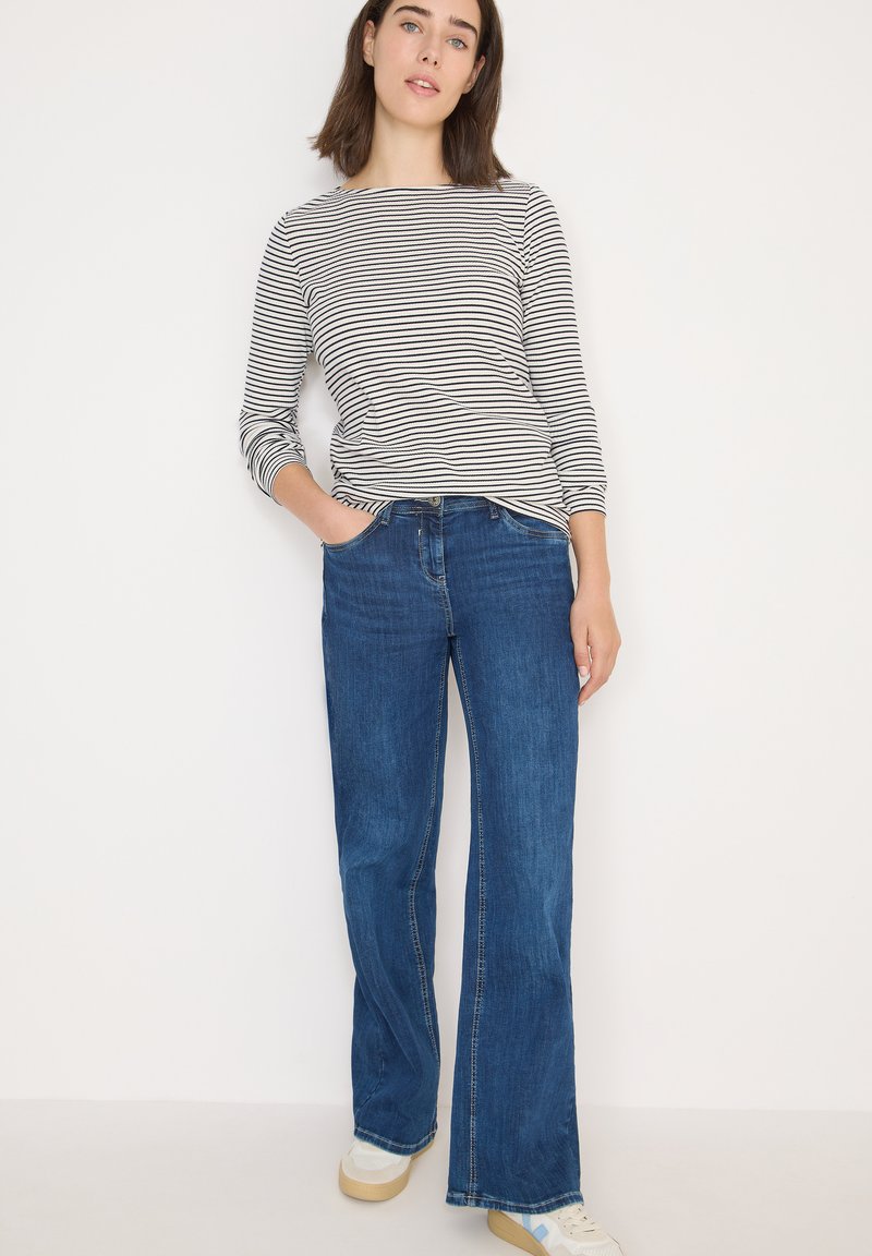 Gestreepte longsleeve top in zwart en wit; blauwe wijde jeans met een klassieke pasvorm; lichtgekleurde sneakers; gladde textuur.