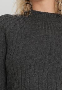 Pull en maille côtelée gris foncé avec un col montant. La texture est douce, présentant des rayures verticales sur tout le tissu.