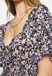 Abito floreale con sfondo nero, caratterizzato da fiori rosa, blu e gialli. Tessuto morbido, maniche corte e design con vita arricciata.