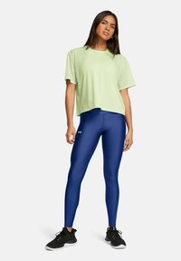 Camiseta de malla verde clara con mangas cortas y cuello redondo, combinada con leggings deportivos azules. Zapatillas deportivas negras completan el conjunto.