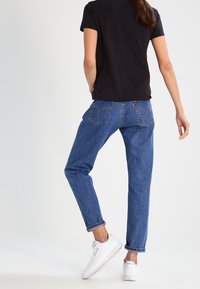 Modré džíny z denimu s volným střihem, vysokým pasem, ohrnutými lemy a klasickými zadními kapsami. Nosené s černým tričkem a bílými teniskami.