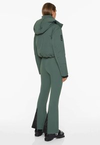 Green puffer jacket with a hood, paired with fitted green pants featuring side slits at the hem. Textured, matte finish, and sleek design.