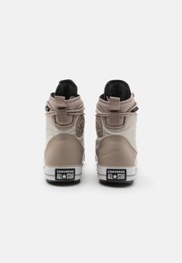 Béžové vysoké tenisky vyrobené z plátna a kůže, s černým interiérem, prošitými detaily a ozdobným logem na zadním podpatku.