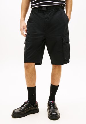 Man draagt zwarte cargo shorts tot op de knie met zijzakken, zwarte sokken en zwarte leren schoenen met dikke zolen.