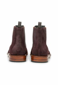 Une paire de bottes chevilles en cuir texturé marron foncé avec des talons en bois empilés et des tirants, présentée de l'arrière sur un fond blanc.