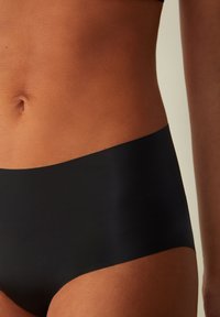 Zwarte naadloze onderbroek met een zachte textuur, lage taille, en gladde randen, weergegeven tegen gebruinde huid.