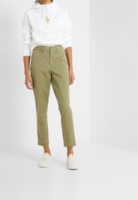 White hoodie with a logo, light olive green tapered pants, and beige sneakers. Simple design, cotton material, casual fit.