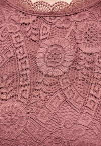 Πολύπλοκο ροζ δαντελένιο ύφασμα με λουλουδάτα και γεωμετρικά σχέδια, που παρουσιάζει λεπτές λεπτομέρειες από δίχτυ και κυματιστές άκρες.