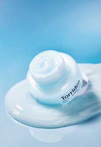 Vaaleansininen Torriden Dive In Soothing Cream -purkki, jossa on sileä geelimäinen rakenne, lepää samanlaisen koostumuksen altaalla.