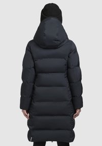 Námornícky dlhý prešívaný kabát s kapucňou, so prešitými časťami, hladkým povrchom a bočnými vreckami. Pletená čiapka dotvára vzhľad.