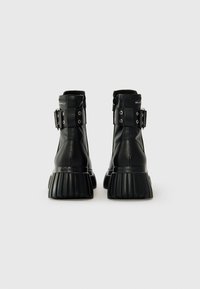 Black leather ankle boots featuring a rounded toe, prominent ribbed sole, and buckle accents on the sides. Zipper closures for easy wear.