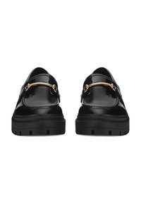 Mustad musta patendiga nahast sussid paksude sooniliste talladega ja kullast metallist ribaga detail ees, vaadatuna seljataha.