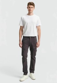 Tumehallidest kangast cargo püksid küljetaskutega, kombineeritud lihtsa valge t-särgiga. Modell kannab valgeid vabaajajalatsid. Lihtne, keha järgiv disain.