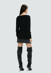 Schwarzer Langarmpullover mit rundem Halsausschnitt, kombiniert mit einem schwarzen Jeansrock und knielangen schwarzen Lederstiefeln mit glänzendem Absatz.