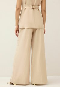 Beige kahden osan asukokonaisuus, jossa on vyöllinen yläosa, jossa on pystysuoria raitoja, sekä leveälahkeiset housut. Sujuva pinta, jossa on vain vähän yksityiskohtia.