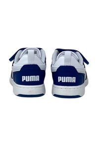 Baskets Puma bleu et blanc avec une tige en cuir lisse, des accents en mesh et une sangle Velcro, présentant un logo bien visible sur le talon.