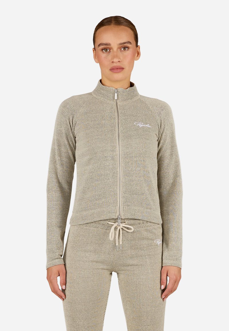 Gai beige krāsas jaku ar rāvējslēdzēju, ar ribotu tekstūru, augstu apkakli un logo akcentu; savienota ar atbilstošām pieguļošām biksēm.