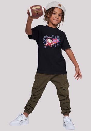 Schwarzes T-Shirt mit einem bunten Grafikdesign eines Cartoon-Charakters und Sternen, kombiniert mit olivfarbenen Cargo-Hosen und weißen Sneakern.