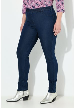 Mörkblå elastiska jeans med slim fit, med sömnadsfickor och en mjuk denimtextur. Kombineras med metallic silverfärgade ankelboots.