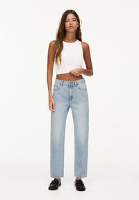 Top in cotone bianco corto abbinato a jeans dritti azzurri chiari. I jeans presentano tasche classiche e una chiusura con bottone e zip standard.