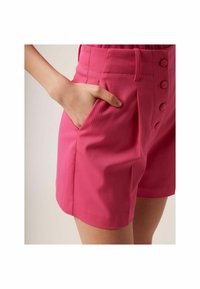 Shorts rose vif à texture lisse, dotés d'une taille haute, de poches avant et d'une rangée de six boutons verticaux.