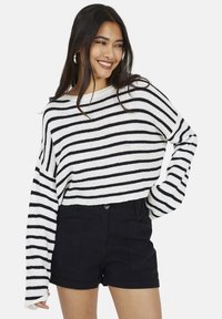 Sweter w paski w białym i czarnym kolorze, z szerokimi r�ękawami i luźnym krojem, zestawiony z czarnymi szortami o wysokim talerzu z przednimi kieszeniami.
