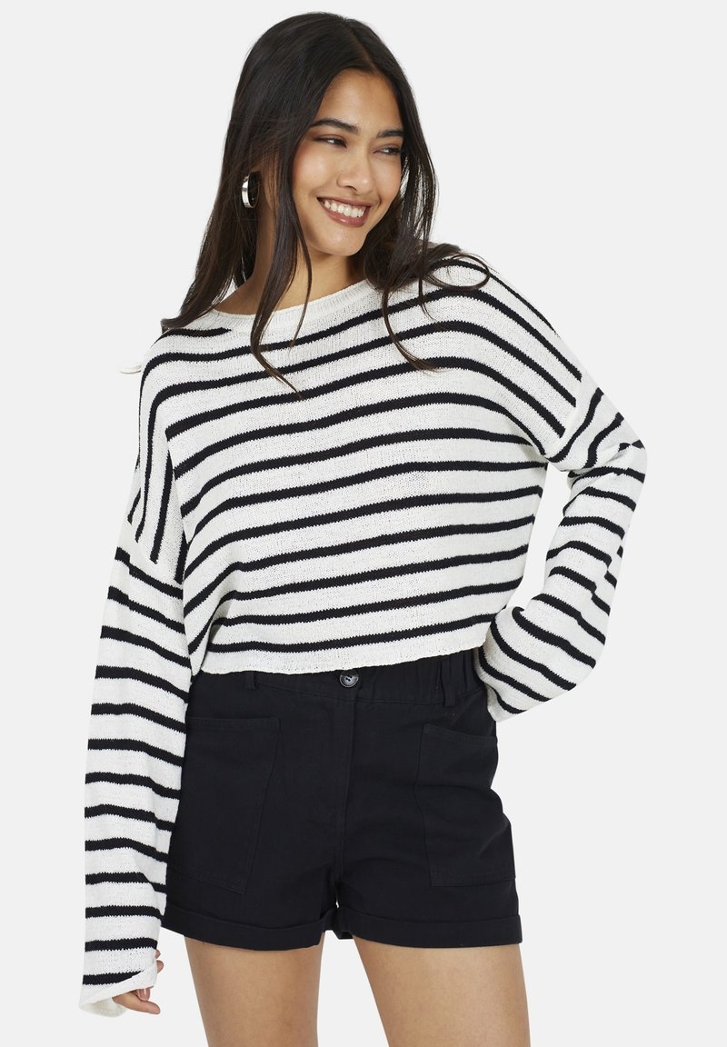 Sweter w paski w białym i czarnym kolorze, z szerokimi rękawami i luźnym krojem, zestawiony z czarnymi szortami o wysokim talerzu z przednimi kieszeniami.