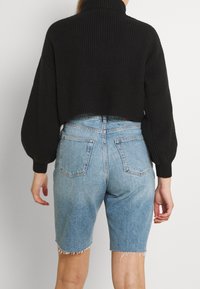 Zwarte geribbelde cropped trui met hoge kraag, gecombineerd met lichtblauwe denimshorts met een onafgewerkte zoom en achterzakken.